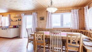 Interior de una cabaña de madera con comedor, cocina y ventanas amplias.