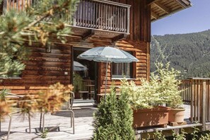 Une cabane en bois dotée d’un balcon, d’un espace extérieur aménagé et offrant une vue sur une montagne boisée.