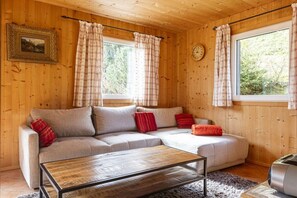 A cozy room with a sofa, a coffee table, and a clock on the wall. - Cabin in Annaberg with swimming pool (Annaberg)