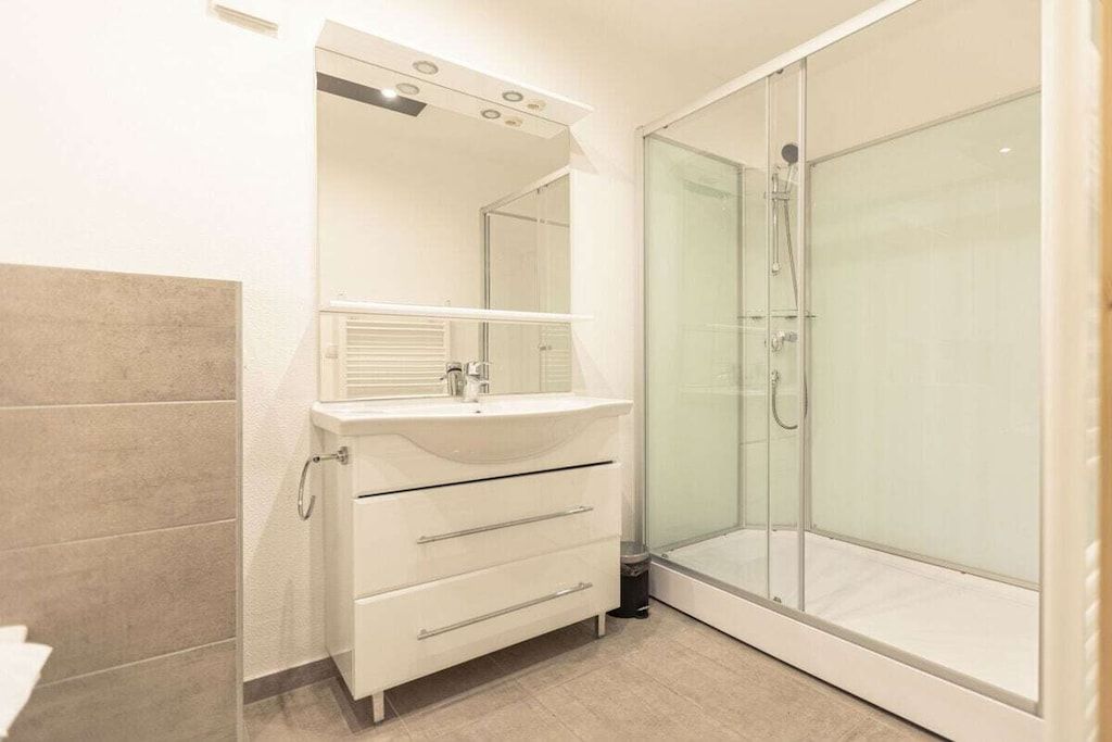 Un bagno con doccia vetro, un mobile lavabo bianco con specchio e pavimento piastrellato.