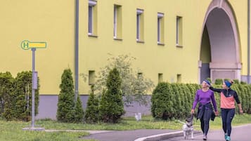 Two people walking a dog on a sidewalk with a yellow building in the background.