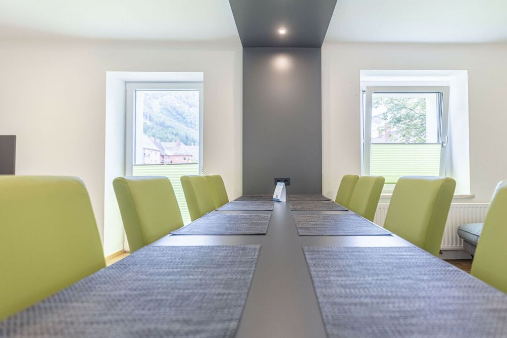 Ein Konferenzraum mit einem langen Tisch, Stühlen, großen Fenstern und einer neutralen Wandfarbe.