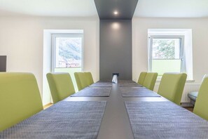 Un salón de conferencias con una larga mesa, sillas y ventanas con persianas.