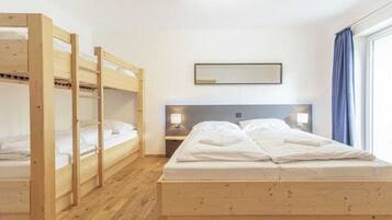 Ein Zimmer mit einem Etagenbett, einem Einzelbett, einem Nachttisch mit Lampe und einem Fenster mit Vorhängen.