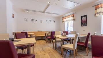 A dining area with wooden tables and chairs, a bench, and a ceiling with recessed lighting.