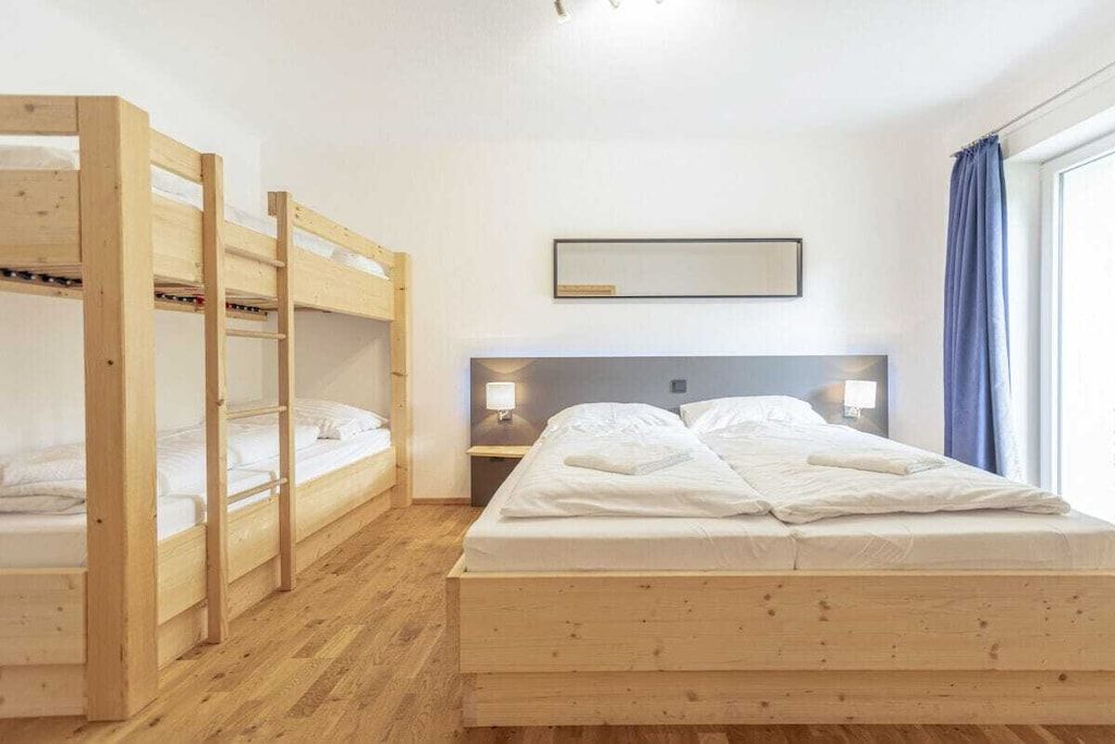 Ein Zimmer mit einem Etagenbett, einem Einzelbett, einem Nachttisch mit Lampe und einem Fenster mit Vorhängen.