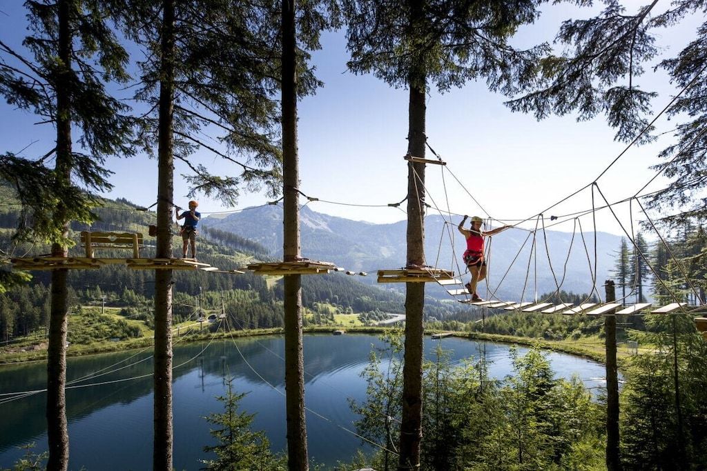 Un ponte sospeso su un lago, con montagne ricoperte da boschi sullo sfondo.