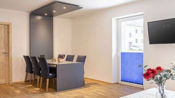 A modern dining area with a table and chairs, a television mounted on the wall, and a door leading outside.