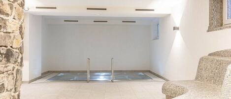 Un área de piscina con una pared de piedra, piso de baldosas y una silla de mosaico.