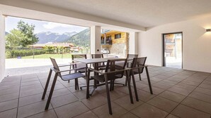Ein Essbereich mit Tisch und Stühlen, Blick auf Berge und ein Gebäude mit einer Stein-Fassade.
