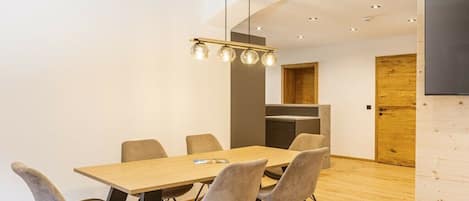 Un comedor moderno con una mesa y sillas de madera, una lámpara colgante y una cocina al fondo.