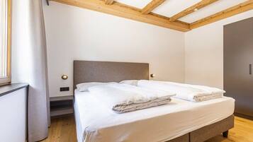 A bedroom with a bed, wooden ceiling beams, a window with curtains, and a wardrobe.
