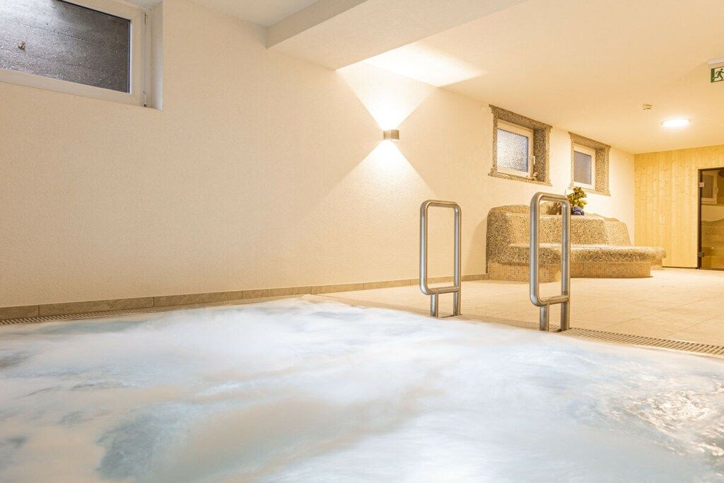 Un área de spa con un jacuzzi, un banco de madera y una lámpara fijada a la pared.