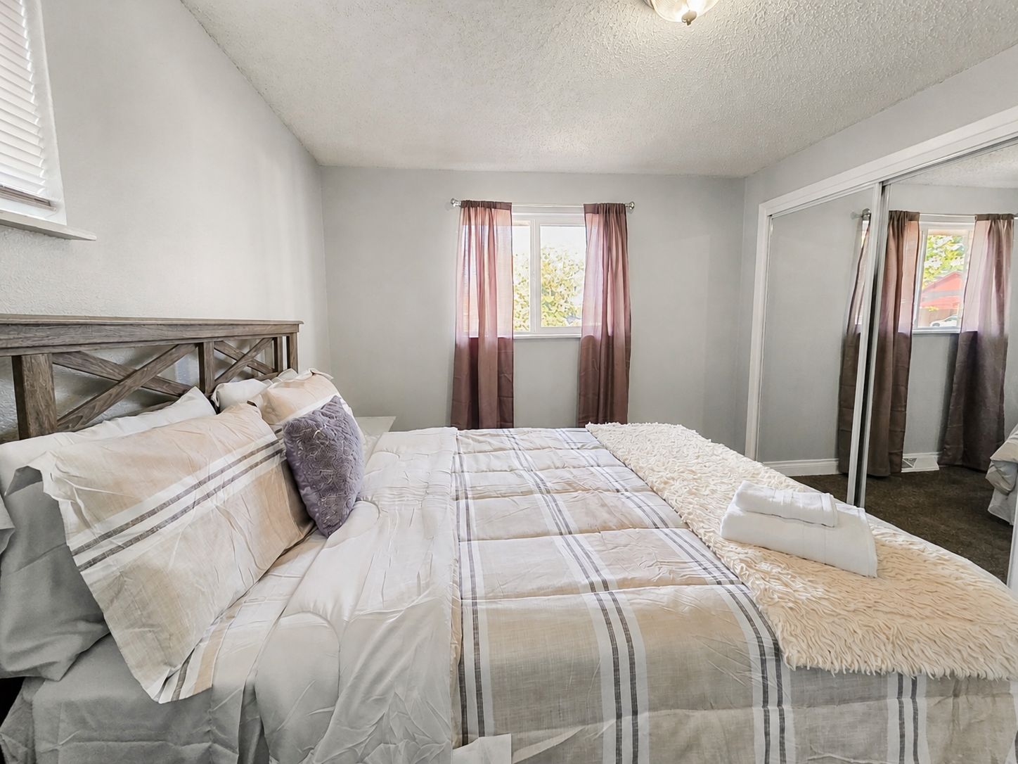 Une chambre à coucher avec un lit, une fenêtre avec des rideaux et un miroir.