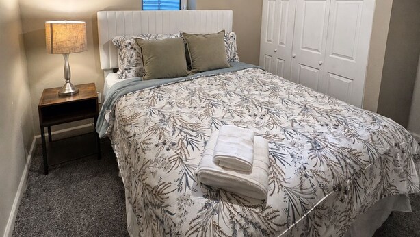 Een slaapkamer met een bed, nachtkastje, lamp, plafondventilator en een raam.