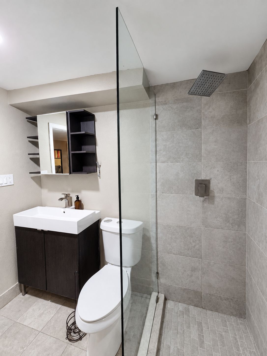 Een moderne badkamer met een douchecabine van glas, een wit toilet en een donkerkleurige wastafel met spiegel erboven.