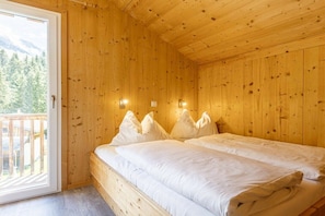 Ein Zimmer in einer Holzhütte mit einem Bett, zwei Wandleuchten und einer Tür zu einem Balkon.