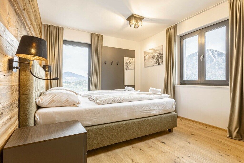A bedroom with a bed, a bedside table, a lamp, a window with curtains, and artwork on the wall.