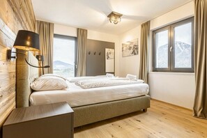 Un dormitori amb un llit, una tauleta de nit, una làmpada, una finestra amb cortines i una obra d'art a la paret.