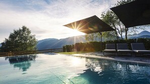Piscina com vista para a montanha, sol brilhando e área de estar coberta.
