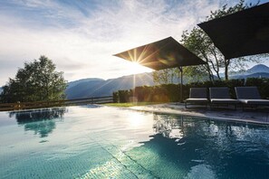Piscina con vista sulle montagne, il sole che splende e un'area relax coperta.