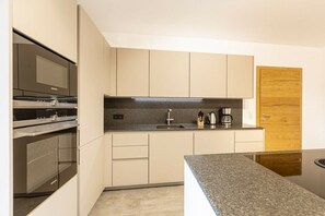 Una cuina moderna amb electrodomèstics integrats, taulell de granit i armaris de colors clars.