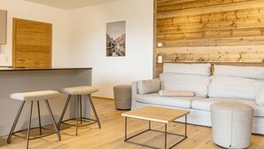 Uma sala de estar moderna com uma parede de destaque em madeira, um sofá, uma mesa de centro e dois banquetas.