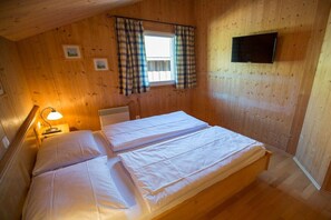 Een kamer met houten lambrisering, een bed, een raam met gordijnen, een wandtelevisie en een bedlampje.