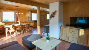 Un interior de madera con zona de comedor, sofá, televisor y armarios.