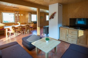 Een houten interieur met een eethoek, een bank, een televisie en kasten.