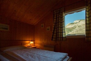 Ein Zimmer mit Holzwänden, einem Bett, einem Nachttisch mit Lampe und einem Fenster mit Vorhängen.
