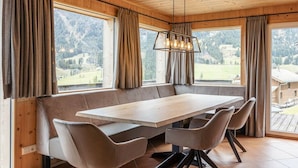 Un interior de madera con una mesa grande y sillas, una lámpara colgante y ventanas amplias con cortinas.