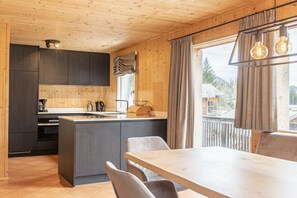 A modern kitchen with a central island, dark cabinetry, and a dining area with a wooden table and chairs. - Cabin in Annaberg with swimming pool (Annaberg)