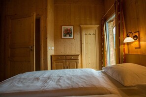Ein Zimmer mit Holzboden, einem Bett, einem Kleiderschrank und einer Wandlampe.