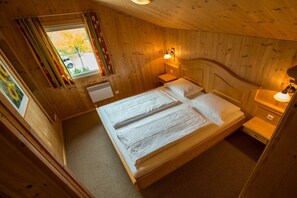 Ein Schlafzimmer einer Holzhütte mit einem Bett, Nachttischen und einem Fenster mit Vorhängen.