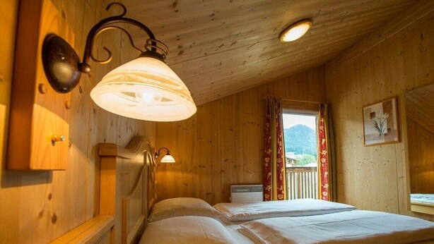 Una habitación de madera con dos camas, una ventana con cortinas y una lámpara fijada a la pared.