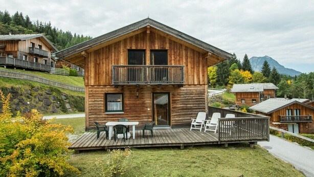 A wooden cabin with a balcony, a deck with chairs, and a mountain backdrop. - Cabin in Annaberg with swimming pool (Annaberg)