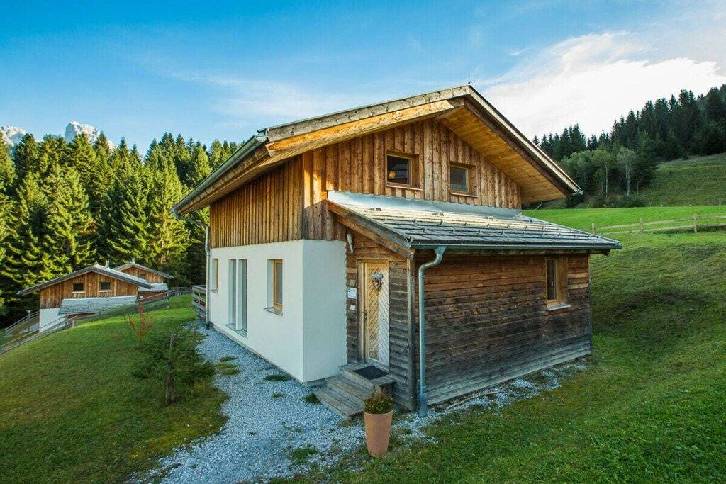 Een houten chalet met een schuin dak, een klein terras en een grindpad.