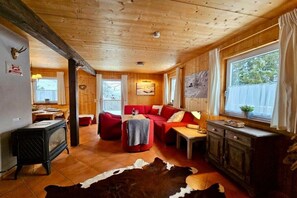 A cabin interior with a wooden ceiling, a red sofa, a dining area, and a kitchen with a stove. - Cabin in Annaberg with swimming pool (Annaberg)