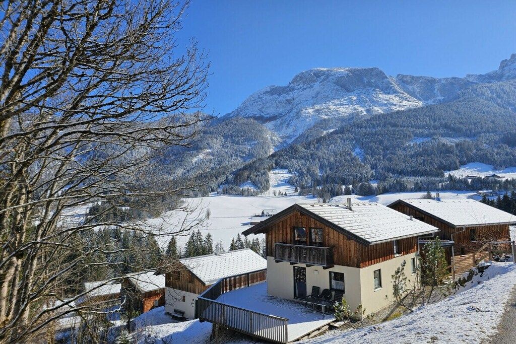 Een chalet met een balkon, omgeven door besneeuwde bergen en bomen.