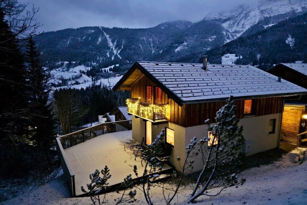 Un chalet en bois doté d’un balcon, entouré de montagnes enneigées.