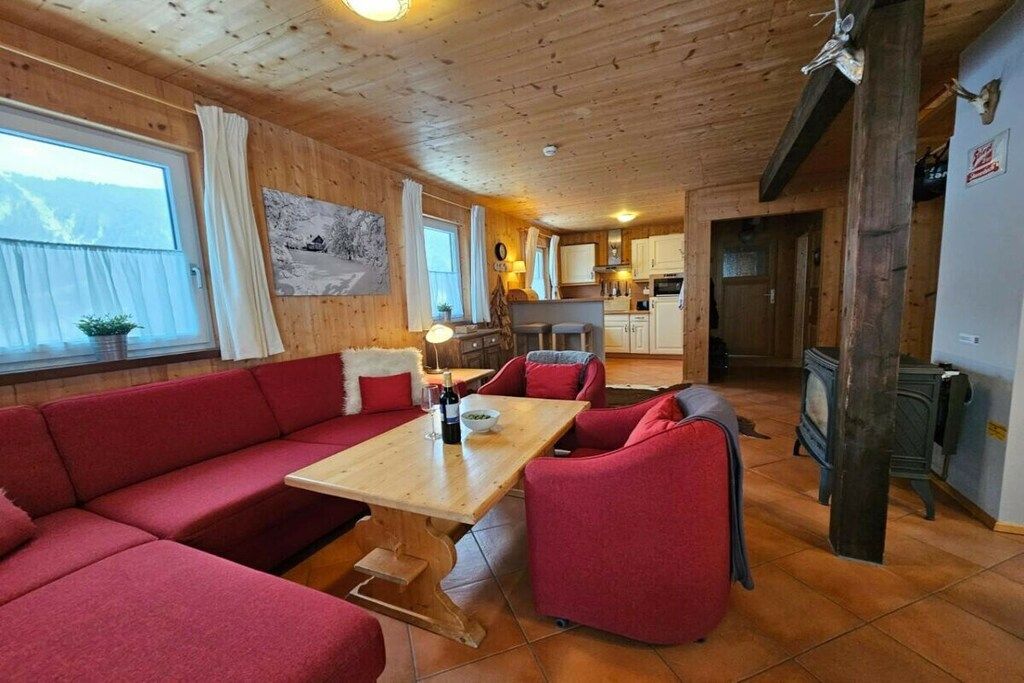Een gezellig cabin interieur met een houten plafond, een eethoek met rode bekleding, een keuken met fornuis en een groot raam met gordijnen.