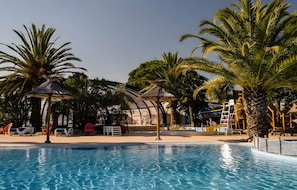 A swimming pool with palm trees, lounge chairs, and a covered seating area. - 5-Star Mobile Home with Shared Pools, Terrace & Private Garden in Saint-Georges-d'Oléron (Saint-Georges-d'Oléron)