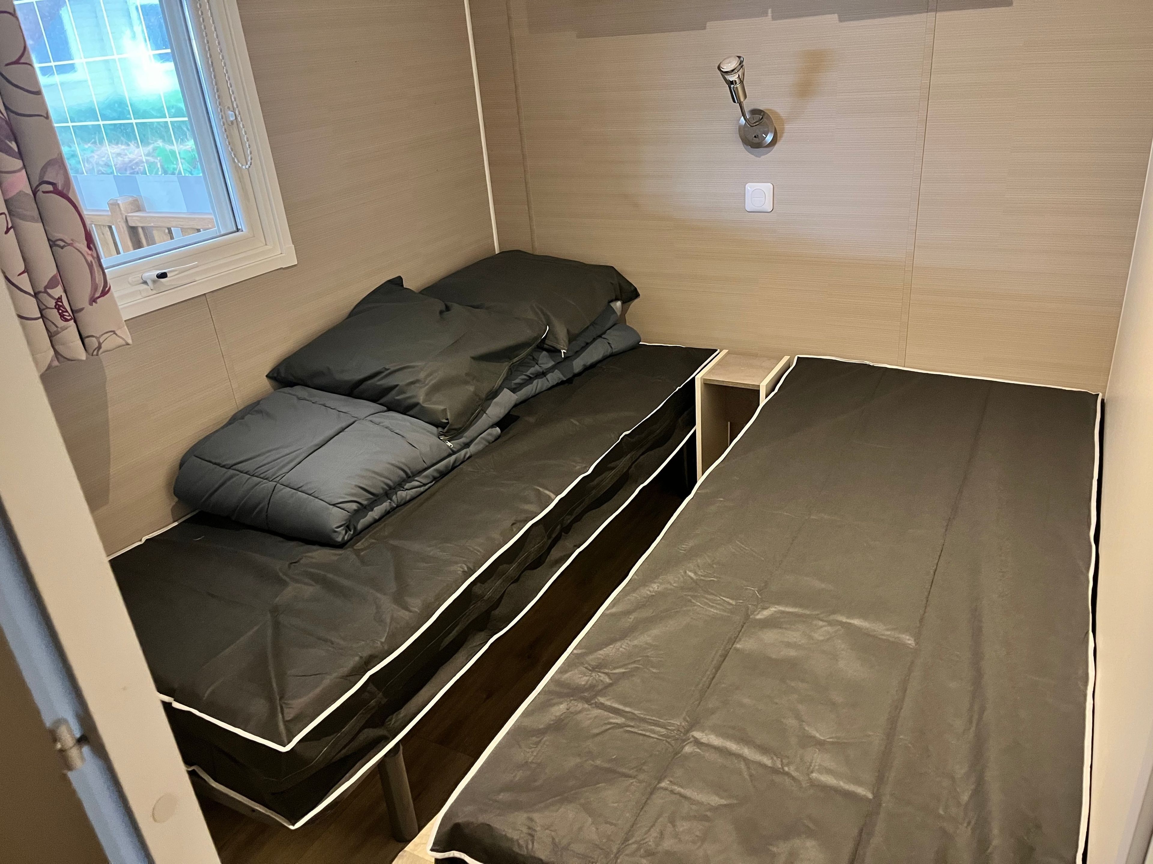Ein kleines Zimmer mit einem Bett, einem Fenster mit Vorhängen und einer Tür.