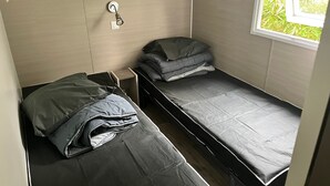 Een kleine kamer met twee eenpersoonsbedden, een klein tafeltje, een wandplank en een raam met uitzicht op groen.