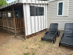 Área externa coberta com deck de madeira, duas cadeiras de descanso pretas e um toldo listrado em branco e cinza.