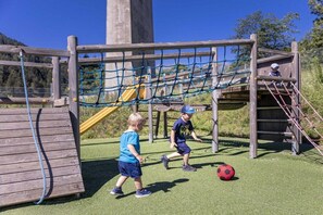Kinderen spelen op een speelplaats met een touwbrug en een glijbaan.