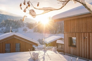 Een houten blokhut met een met sneeuw bedekte dak, omgeven door een besneeerd landschap en bergen.