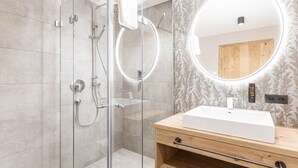 Een moderne badkamer met een glazen douchecabine, een houten wastafelmeubel en een ronde spiegel met verlichting.