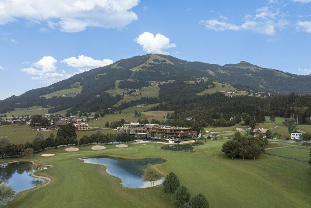 Een golfbaan met een berg op de achtergrond, een clubhuis en een klein vijvertje.